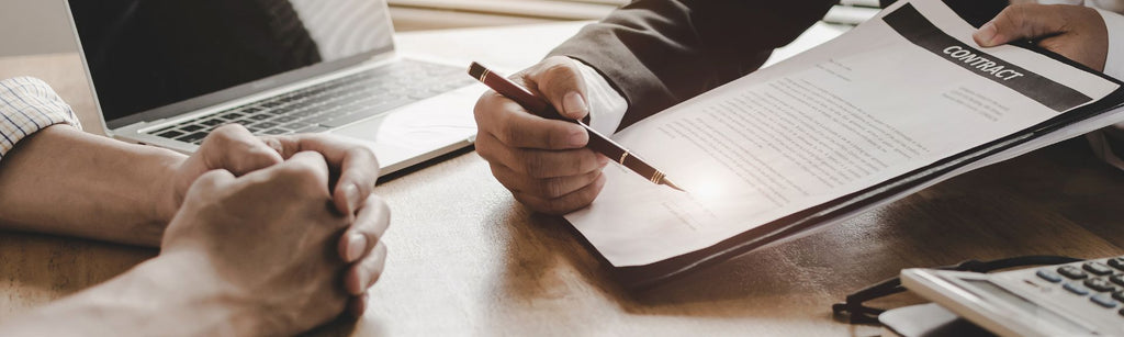Two people meeting over paperwork,  one pointing to a signature field with a pen while wearing a suit, closeup on their hands only