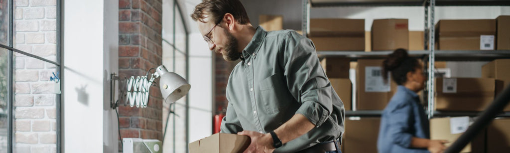 Two people inside of an office with boxes in the background.