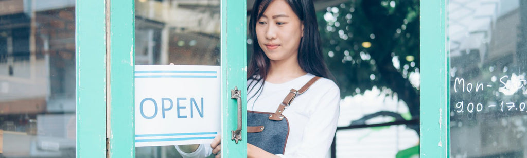 Woman in overalls stands behind blue door with OPEN sign